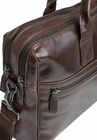 Brązowa skórzana torebka posiada podwójne suwaki, regulowany pasek, gładką fakturę i przednią kieszeń z suwakiem. Wykończona srebrnymi metalowymi elementami.