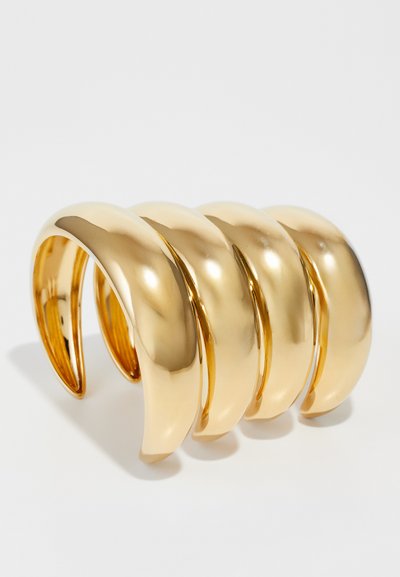 Gold-tone metal cuff bracelet featuring a wave-like design with four smooth, interlocking sections. Highly reflective surface with rounded edges.