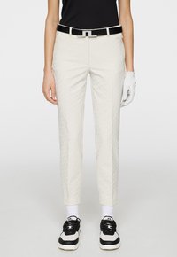 Cream golf pants with a textured pattern, slim fit, and ankle length. Paired with a black belt and black-and-white athletic shoes.