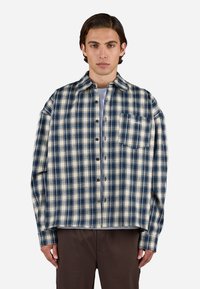 Flannel skjorte i creme og marineblå tern med spids krave, knaplukning og en brystlomme. Blød tekstur, afslappet pasform.