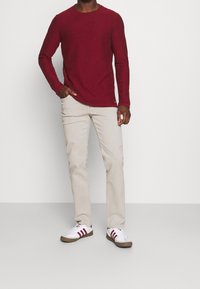 Röd långärmad skjorta med rund halsringning, i kombination med beige byxor och vita sneakers med vinröda ränder. Enkel design, avslappnad passform.