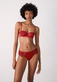 Czerwony zestaw bielizny składający się z balkonetki z kwiatowym koronkowym wykończeniem oraz dopasowanych majtek z koronkowymi akcentami wzdłuż linii talii.