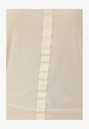 Haut beige avec un détail de ruban en satin vertical et des plis. Le tissu semble lisse et léger, créant une texture douce.