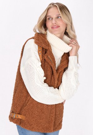 Bruine fleece vest met een textuurovervlak, voorzien van een hoge kraag, rits en leren accenten in bruin. Witte gebreide trui met kabelpatroon.
