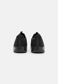 Zapatillas deportivas negras con parte superior de malla, tirador y suelas de goma texturizadas, que presentan un diseño elegante y minimalista con acentos en contraste.