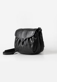 Borsa a spalla in pelle nera con forma arrotondata, texture morbida, patta pieghevole e chiusura a scatto. Include una tracolla regolabile.