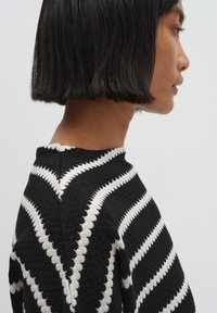 Zwart-witte trui met zigzagpatroon, gestructureerde stof, ronde hals en zichtbare naden, weergegeven vanuit een zijaanzicht.