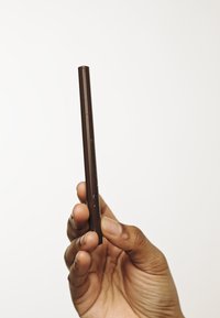 Un stylo à encre marron tenu verticalement dans une main, présentant un corps cylindrique lisse et une pointe fine, avec une finition mate.