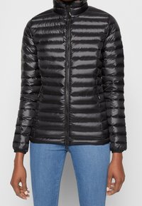 Sort foret jakke med lynlås foran, vandret quiltet design og høj krave. Glat, skinnende stof med elastiske manchetter.