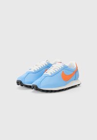 Scarpe da ginnastica in rete blu con dettagli arancioni e lacci bianchi. Presentano una punta arrotondata, una suola imbottita e un fondo in gomma nera con trazione.