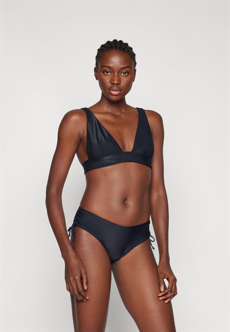 Set bikini nero con bralette triangolare a coste con spalline larghe e slip a vita bassa abbinati con lacci laterali regolabili.