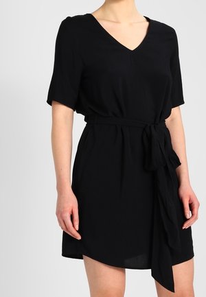 Robe noire avec un décolleté en V, des manches courtes et une ceinture à nouer. Réalisée en tissu lisse, présentant une coupe décontractée et un ourlet asymétrique.
