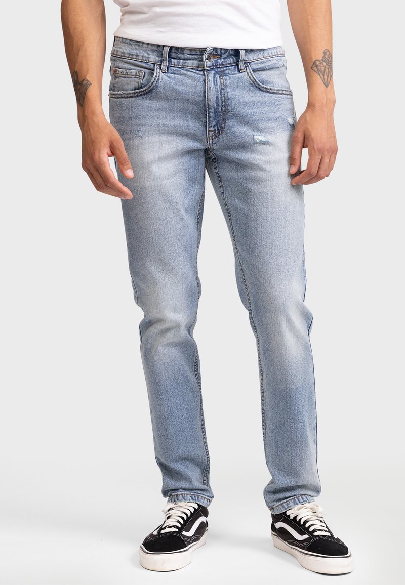 Lyseblå denimjeans med klassisk passform, lett slitasje på lårene og fem lommer; kombinert med svart og hvite sneakers.