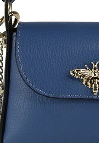 Blauwe leren handtas met een gestructureerde afwerking, gouden bijenembleem op de klep en een kettingriem. Heeft een stijlvolle, rechthoekige vorm.