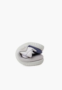 Scarpe pieghevoli con un soffice esterno grigio, imbottitura bianca e un accento blu. La suola in gomma texturizzata è flessibile e compatta.