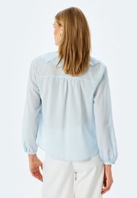 Lichtblauwe blouse met lange mouwen en een relaxte pasvorm, met een ronde kraag, knoopmanchetten en een zachte, textuurvolle stof.