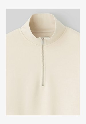 Sweatshirt zippé beige clair avec un col haut, texture douce et poignets côtelés. Doté d'une fermeture éclair métallique au centre devant.