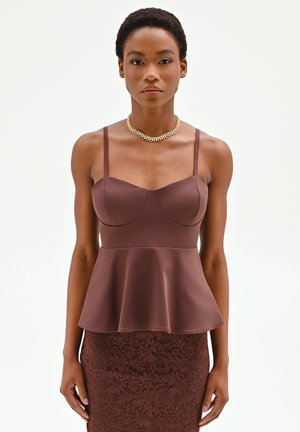 Donna che indossa un top marrone aderente con peplo e sottili spalline, abbinato a una gonna in pizzo floreale, accessoriata con una collana a catena dorata.