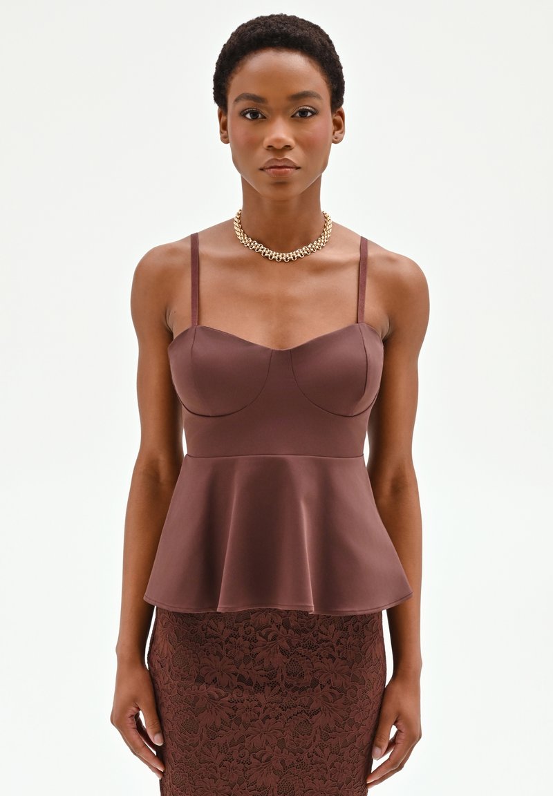 Mujer con un top peplum marrón ajustado con tirantes finos y una falda de encaje floral a juego, complementada con un collar de cadena dorada.