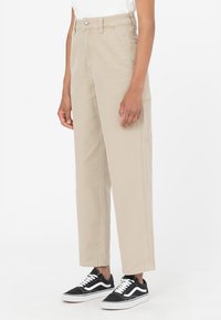 Beiga cargobyxor med rak passform, med sidofickor och kontrasterande sömmar, i kombination med svarta sneakers. Slätt bomullsmaterial.