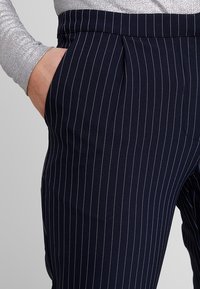Marineblau gestreifte Hose mit schmaler Passform, flachem Vorderteil, Seitentaschen und texturiertem Bund.