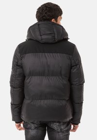 Schwarze Pufferjacke mit abnehmbarer Kapuze, versehen mit genähten horizontalen Abschnitten, strukturiertem Stoff und gerippten Bündchen.