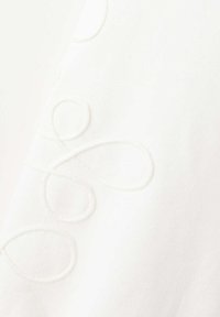 Tissu blanc avec une broderie en relief subtile dans un motif floral abstrait en boucle créant une texture douce à la surface.
