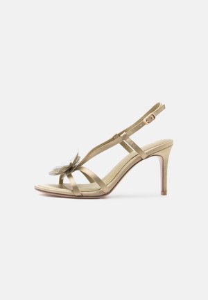 Guld sandal med høje hæle med tynde stropper, justerbar spænde, åben tå og dekorativ gennemsigtig blomst på forreste strop.