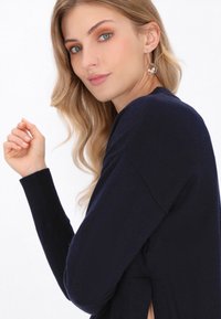 Pulover bleu marin cu mâneci lungi și o croială lejeră, având o fante laterală și manșete cu elastan. Modelul poartă cercei rotunzi cu perle.