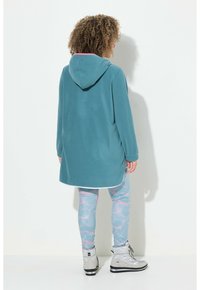 Teal huppari, jossa on vaaleanpunainen vuori hupussa, yhdistettynä vaaleansinisiin legginsseihin, joissa on vaaleanpunainen marmorikuvio ja harmaat saappaat.