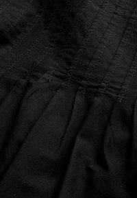 Tissu noir avec des plis, présentant des lignes de couture visibles. La texture est lisse et douce, avec un léger brillant dans certaines zones.