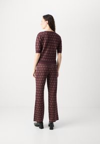 Bordeaux gemustertes Co-Ord-Set mit einem kurzärmeligen Oberteil und Schlaghosen, die ein Diamantdesign und strukturierte Akzente aufweisen. Elastischer Bund.