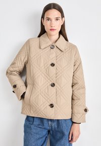 Beige quilted jacket with a large collar, diamond pattern, and four brown buttons. Cuffs feature buttoned details; pockets are visible on the sides.