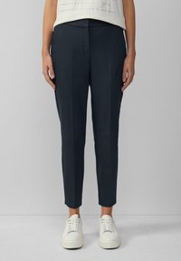 Pantalons tailleur bleu marine à coupe ajustée, dotés de poches latérales et d'une texture lisse, associés à des baskets blanches pour créer un contraste.