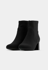Černé kotníkové boty vyrobené z hladkého materiálu, s přiléhavým designem, zaoblenou špičkou a širokým podpatkem s matným povrchem.