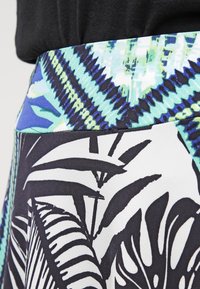 Jupe à motif floral avec une large ceinture en vert et bleu, contrastant avec un design de feuilles noir et blanc. Le matériau semble lisse.