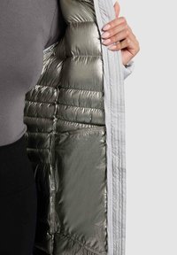 Lehká prošívaná bunda s elegantním stříbrným kovovým vnitřkem, bílým vnějším materiálem, prošívanou strukturou a přiléhavým střihem.