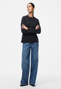 Μαύρο μπλουζάκι με μακριά μανίκια σε συνδυασμό με φαρδιά μπλε τζιν παντελόν�ια. Το σύνολο χαρακτηρίζεται από έναν απλό σχεδιασμό και λεία υφή. Μαύρα υποδήματα ολοκληρώνουν την εμφάνιση.