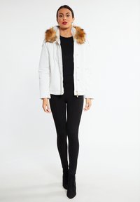Hvid pufferjakke med faux fur hætte, guld hardware accenter og lynlåslukning, parret med sorte leggings og ankelsko.