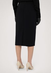 Svart pennkjol med en bakslits, bärs med beige högklackade skor. Långa svarta handskar framhäver outfiten. Minimalistisk design och slät textur.