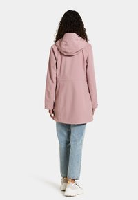 Roze waterdichte jas met een capuchon, ontspannen pasvorm, knie-lange ontwerp en drukknopen, gecombineerd met lichtblauwe rechte jeans en sneakers.