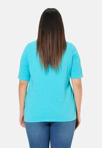 Camiseta de manga corta color turquesa, hecha de una tela suave, con un corte holgado y un escote redondeado. Se lleva con jeans azules.
