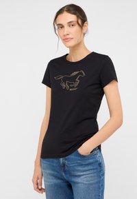 Juodas medvilnės marškinėliai su trumpomis rankovėmis, su auksiniu žirgo piešiniu ant priekio. Pora su mėlynais džinsais.