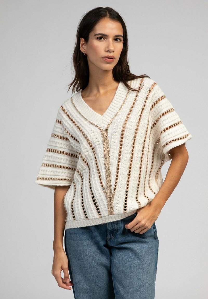 Pull en tricot à manches courtes crème, présentant un col en V, des motifs rayés avec des découpes, et une coupe décontractée. Assorti à un jean bleu.