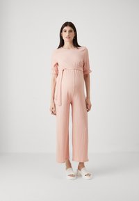 Rosa teksturert jumpsuit med pufferm og knyttet midje. Vid buksebein design kombinert med hvite platåsandaler. Enkel, elegant look.