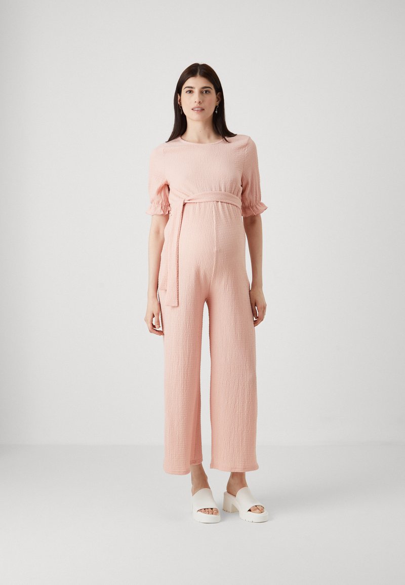 Rosa teksturert jumpsuit med pufferm og knyttet midje. Vid buksebein design kombinert med hvite platåsandaler. Enkel, elegant look.