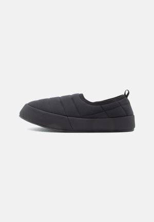 Sorte slip-on sko med quiltet stof, der har en struktureret overflade, rund tå og gummisål. Inkluderer en baglæns trækstrop for nem påføring.