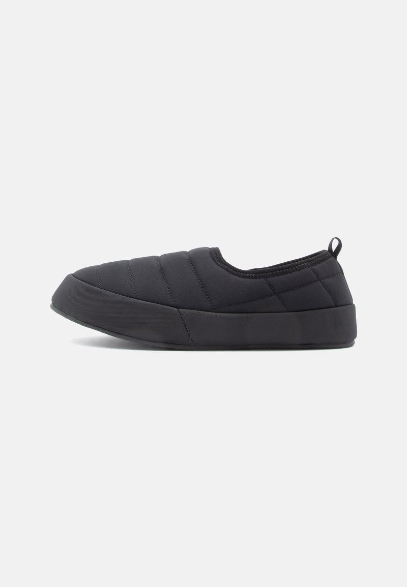 Black slip-on shoes featuring quilted fabric with a textured surface, rounded toe, and a rubber sole. Includes a rear pull tab for easy wear.