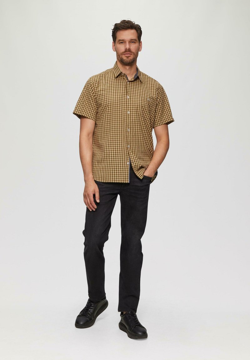 Korte mouwen, geruit overhemd in bruin en beige, met knoopsluiting. Gecombineerd met donkere jeans en zwarte sneakers. Eenvoudige, casual stijl.
