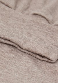 Gant de tricot beige doux avec poignet en côtes, montrant une texture de tissu détaillée et des doigts repliés.
